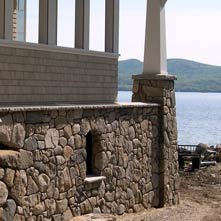 Tightly fitting fieldstone veneer on the exterior of a New Hampshire lake house with custom granite coping