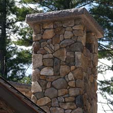 Custom chimney with tomahawk design crafted out of New England fieldstone with raised 6 thick granite cap