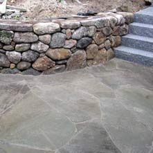 Curved fieldstone retaining wall with large irregular shaped bluestone patio & granite steps
